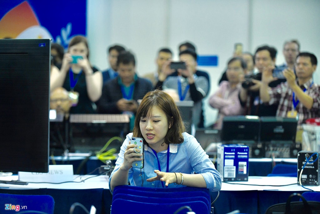 Một phóng viên nữ đã nhanh tay phát trực tiếp (livestream) qua điện thoại đồng thời tường thuật khung cảnh bên trong trung tâm báo chí, trong khi các phóng viên khác lấy máy ảnh chụp lại màn hình TV. Ảnh: Quỳnh Trang.