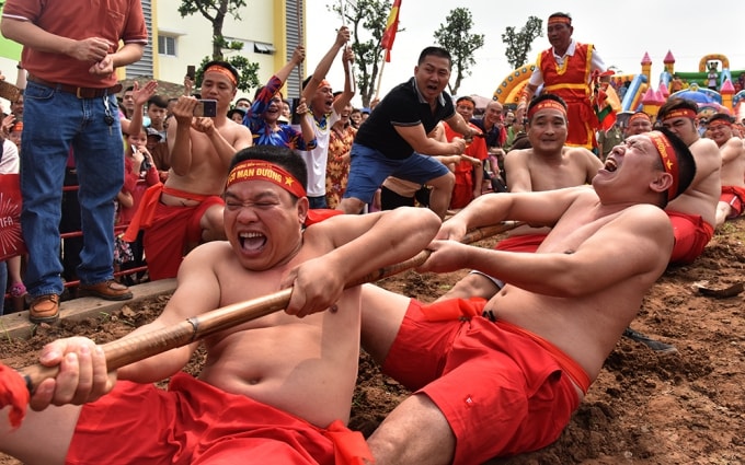 Mỗi đội kéo co từ 15, 17 hoặc 19 người tùy theo từng năm và có một Tổng cờ. Trai kéo co cởi trần, mặc quần ngắn, buộc thắt lưng đỏ, đầu chít khăn đỏ in tên từng mạn. Ảnh: Báo Nhandan