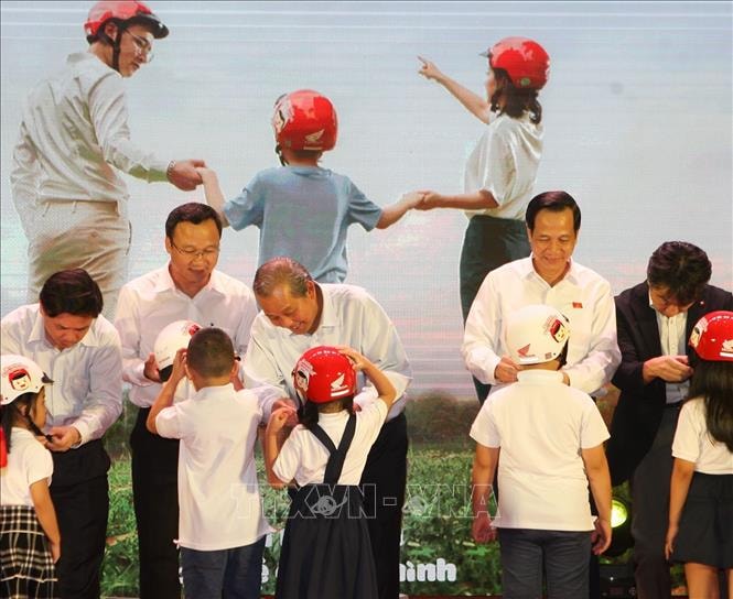Phó Thủ tướng Trương Hòa Bình và các đại biểu trao tặng mũ bảo hiểm cho các em học sinh lớp 1. (Ảnh TTXVN)