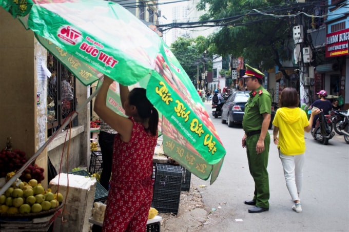 Chiến sỹ Cảnh sát trật tự CAQ Thanh Xuân nhắc nhở người dân thu dọn đồ đạc ô dù lấn chiếm hành lang giao thông.