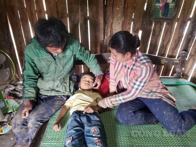 Vợ chồng anh Biêng và chị Xun bận bộ áo quần còn dính bùn đất ngồi nhìn con lên cơn đau mà lòng quặn thắt. Ảnh: Cái Văn Long.