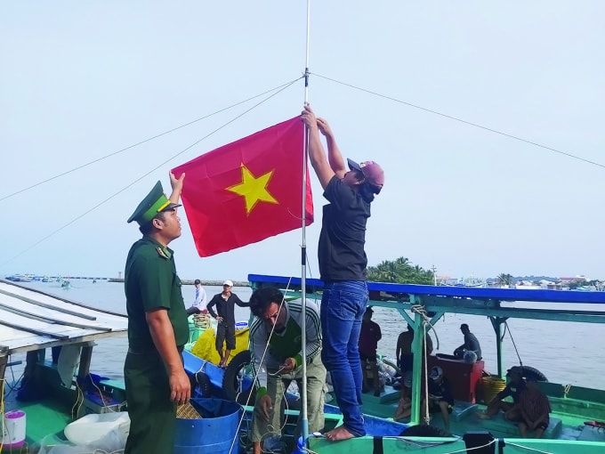 Cán bộ Đồn Biên phòng Cửa khẩu Cảng Dương Đông, huyện Phú Quốc, tỉnh Kiên Giang giúp ngư dân treo cờ Tổ quốc lên tàu – Ảnh: Hoàng Tuấn.