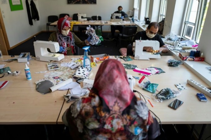 Các người dân nhập cư đang chung tay làm khẩu trang để giúp đỡ cộng đồng - Ảnh: AFP