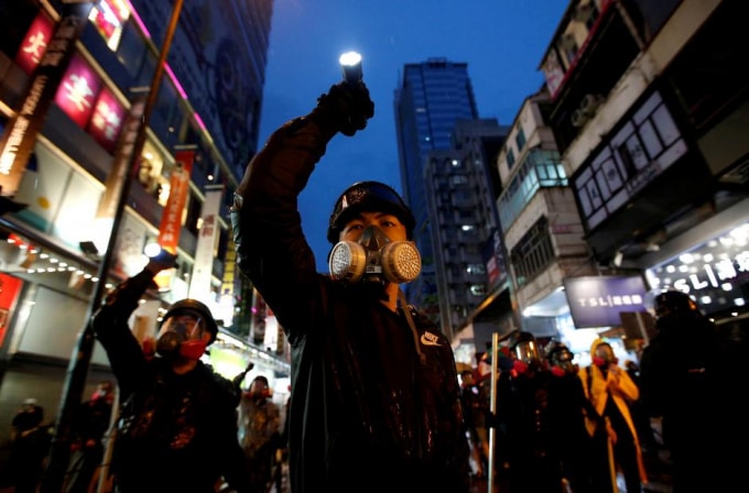Một người biểu tinh đeo mặt nạ cầm đèn pin biểu tình ở Hong Kong. Ảnh: Reuters