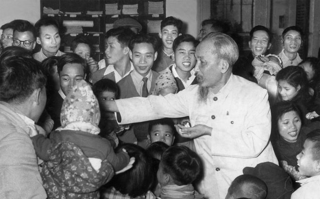 Bác Hồ phát kẹo cho con em những người làm Báo Nhân Dân tại trụ sở 71 Hàng Trống (nghệ sĩ Trịnh Hải đeo cà-vạt đứng cạnh Bác). Ảnh: Nguyễn Kim Côn.