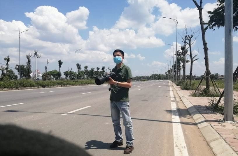 Nhà báo, phóng viên ảnh Phạm Hùng tác nghiệp trên một trục đường giao thông ngoại thành Hà Nội.