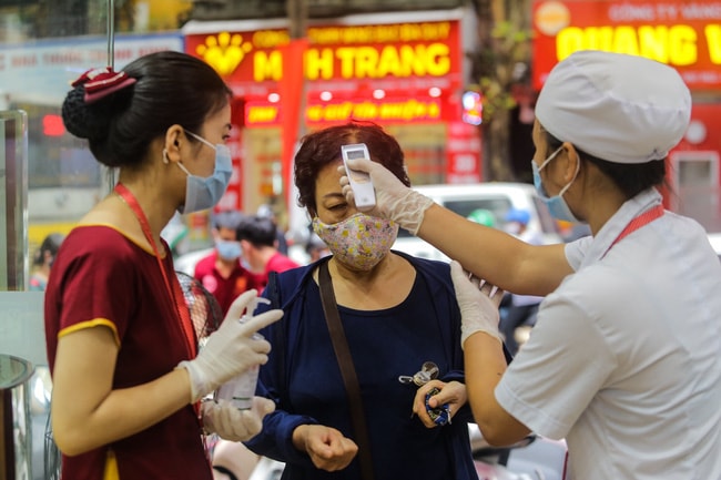 Nhân viên cửa hàng vàng thực hiện đo nhiệt độ, sát khuẩn tay cho khách đến cửa hàng. Ảnh: TL.