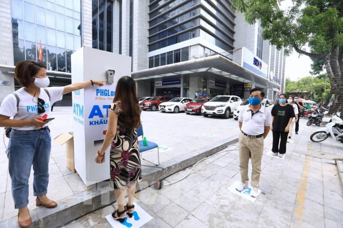 Người dân xếp hàng giãn cách đến lấy khẩu trang tại cây ATM phát khẩu trang miễn phí trên phố Lạc Trung, Hà Nội. Ảnh: Thành Đạt