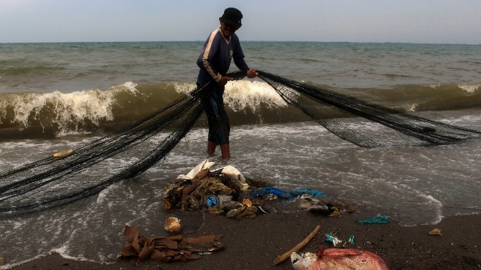 Một ngư dân ở Indonesia tìm kiếm lưới đánh bắt của mình trên một bãi biển đầy rác thải nhựa. Các thiết bị đánh bắt bị bỏ đi đã trở thành mối đe dọa nghiêm trọng đối với môi trường. Ảnh: Getty