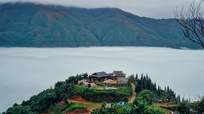 Một ngôi nhà nằm trên ngọn núi, xung quanh là 1 làn mây trắng.