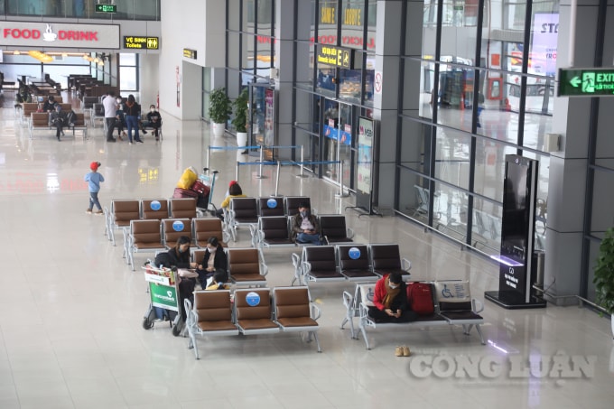 Một vài hành khách ngồi chờ ở sảnh ga sân bay, với rất nhiều hàng ghế trống khách ngồi.