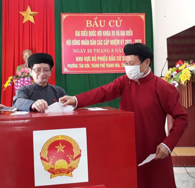Anh Lê Việt Dũng (phải), cán bộ Ban Dân tộc tỉnh Thanh Hóa mặc áo dài ngũ thân đi bầu cử tại phường Tân Sơn, TP. Thanh Hóa. Theo anh Dũng, đây là cách để anh thể hiện tình yêu đối với các giá trị văn hóa truyền thống. Ảnh: FBNV