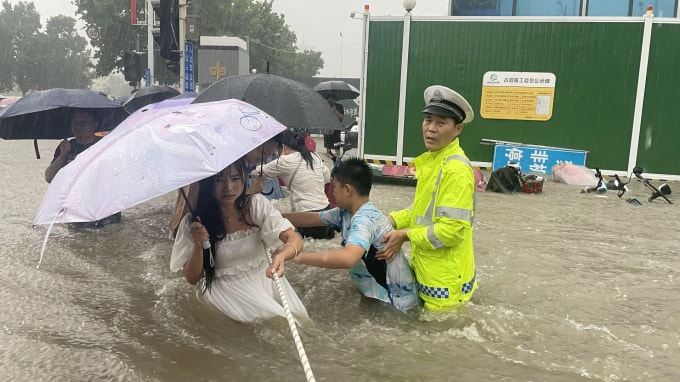 Một cảnh sát giao thông hướng dẫn người dân băng qua con đường ngập nước bằng dây thừng trong trận mưa lớn ở Zhengshou, tỉnh Hà Nam, Trung Quốc ngày 20 tháng 7 năm 2021 - Ảnh: Reuters