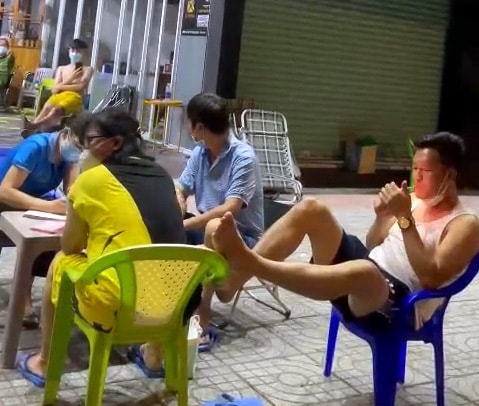 Cơ quan chức năng lập biên bản, nhưng các đối tượng vẫn bất hợp tác. Có một người còn tháo khẩu trang, hút thuốc và gác chân khi làm việc. Ảnh cắt từ clip.